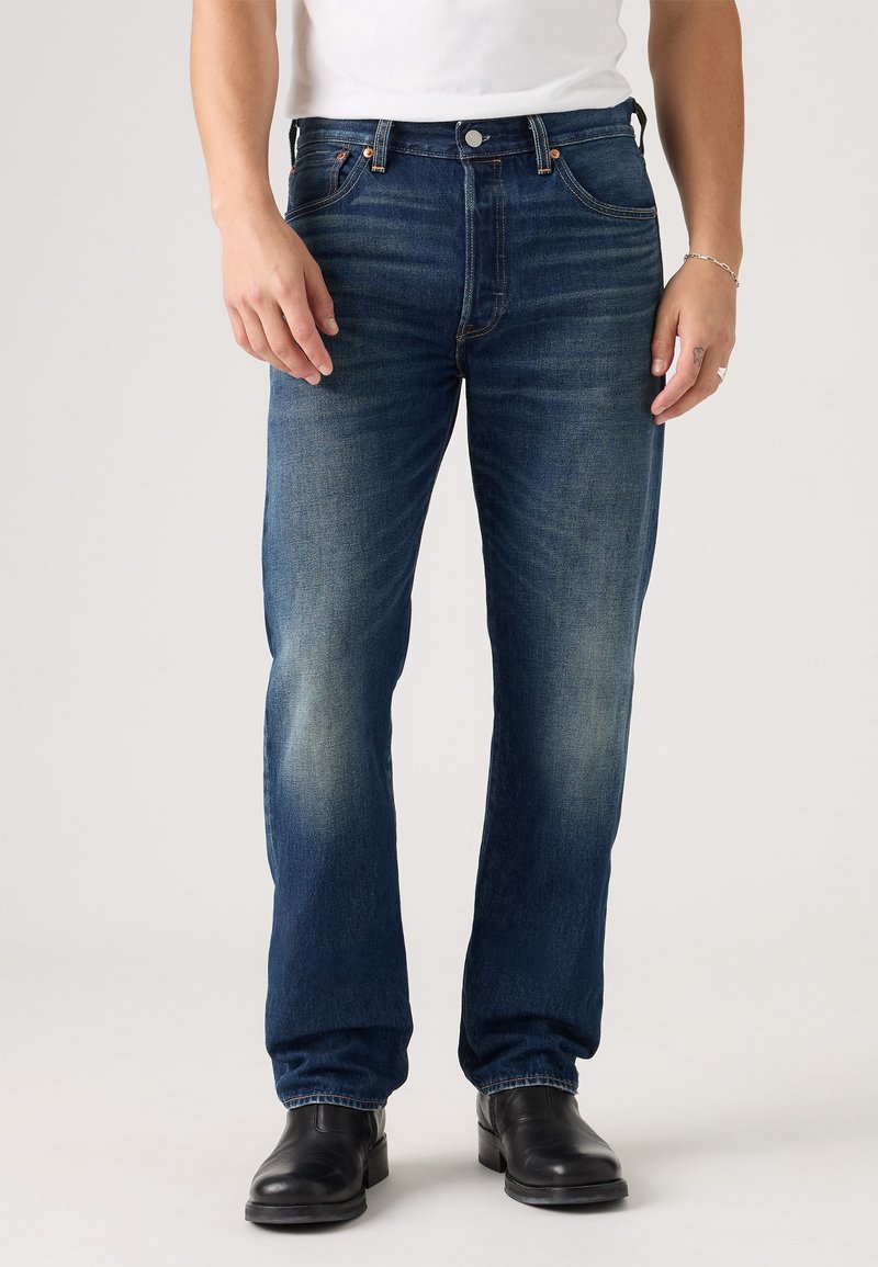 Blå denimjeans med en lett falming, rett snitt, subtile søm-detaljer, fem lommer og metallbeslag. Brukt med svarte støvler.