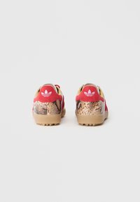Sneaker rossi e beige con un design a stampa serpente testurizzata sul tallone, una suola in gomma liscia e il logo iconico sul retro.