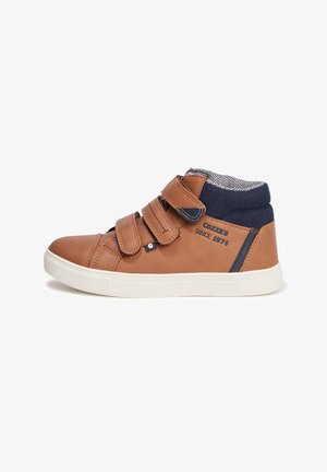 Bottes montantes en cuir marron avec trois bandes Velcro, semelle blanche, col en tissu bleu marine et doublure à motif. "Creek's depuis 1974" imprimé sur le côté.