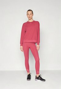 Rosa sportliches Sweatshirt mit Rundhalsausschnitt, kombiniert mit passenden Leggings. Strukturierter Stoff; schwarze Sportschuhe komplettieren das Outfit.