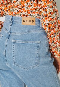 Jasnoniebieskie dżinsy z wysokim stanem z brązową skórzaną metką NA-KD na tylnej gumce oraz dwoma standardowymi tylnymi kieszeniami.