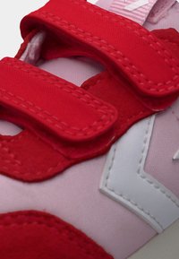 Κοντινή λήψη ροζ αθλητικού παπουτσιού με κόκκινους ιμάντες βέλκρο και λευκή κεντημένη λεπτομέρεια λογότυπου.