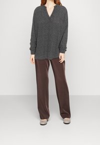 Blusa a maniche lunghe di un grigio scuro con motivo a V, abbinata a pantaloni a gamba larga marroni e ballerine grigio chiaro. Texture morbide in tutto.