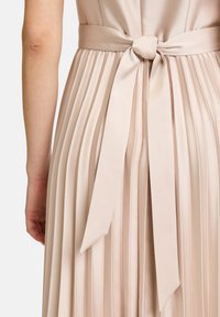 Faltenkleid aus satin in hellem Beige mit einer gebundenen Schleife an der Taille. Verfügt über eine weiche Textur und vertikale Falten für zusätzlichen Dimensionseffekt.