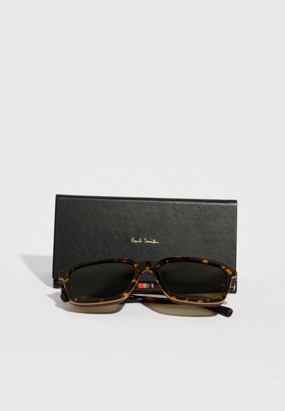 Teknősbarna napszemüveg sötét lencsékkel, téglalap alakú kerettel. Tartozéka egy fekete bőr tok, amelyen a "Paul Smith" felirat dombornyomott.