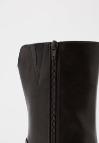 Bota de cuero sintético marrón con cremallera lateral, que presenta costuras verticales y una textura suave. El diseño incluye un ligero corte angular en la parte superior.