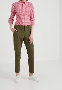 Červeno-bílá kostkovaná košile s dlouhými rukávy, spárovaná s olivově zelenými kalhotami a bílými teniskami.