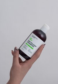 Brun shampooflaske med et hvidt låg, der har en hvid etiket med grøn tekst. Indeholder 250 ml og er mærket til hårstyrke.