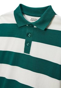 Polo rayé vert et blanc avec un col, trois boutons et une texture en coton lisse. L'étiquette indique "MONOPRIX."
