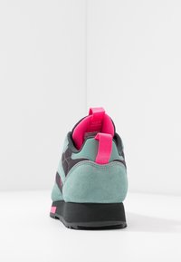 Zelená semišová teniska s růžovými akcenty, texturovaným síťovaným svrškem a zadním poutkem. Podešev je černá s vzorem pro záběr.