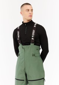 Groene waterdichte overall met verstelbare zwarte banden met witte logo, ritszakken, gladde textuur en aansluitend ontwerp.