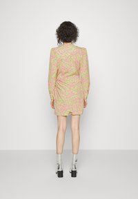 Vestido curto em tecido estampado com corações rosa neon num fundo verde claro. Mangas longas e detalhe franzido nas costas.