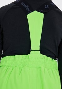 Salopette verde brillante con spalline nere regolabili. Presenta una vita elasticizzata con texture arricciata, progettata per un uso pratico.
