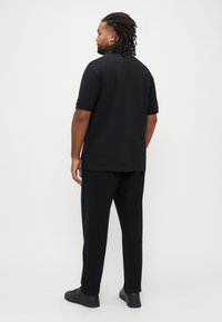 Čierne polo tričko s krátkym rukávom s voľným strihom, v kombinácii s čiernymi nohavicami a čiernymi teniskami, predstavujúce jednoduchý dizajn.