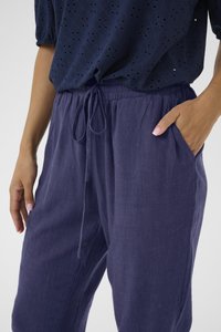 Pantaloni in lino leggeri di colore blu navy, con una vestibilità rilassata, vita con cordoncino, tasche laterali e una texture sottile. Indossati con un top con motivo.
