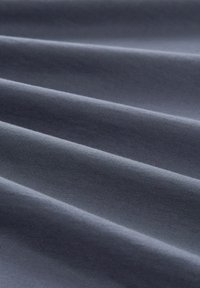 Tmavě modrá látka s viditelnou texturou a záhyby, vyrobená z hladkého materiálu, s jemným šitím a měkkým, pravidelným tkaním.