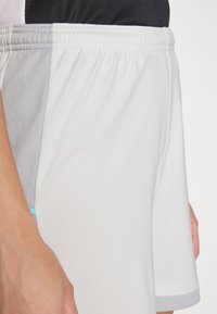 Weiße sportliche Shorts mit elastischem Bund, Netzseiteneinsatz und einem kleinen türkisfarbenen Akzent am Saum. Weicher Stoff mit glatter Textur.