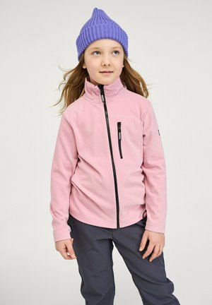 Veste en polaire rose avec un col haut, poche zippée et accents noirs, associée à un pantalon gris et un bonnet en tricot violet.