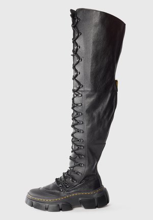 Zwart leren veterschoenen tot de knie met een chunky rubberen zool, voorzien van een gestructureerde afwerking en gele stiksels.