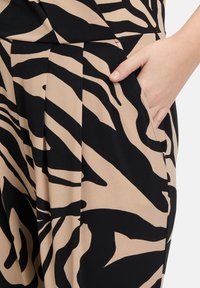 Jumpsuit nero e beige con ampia stampa di tigre, tessuto testurizzato e tasche laterali. Il design plissettato aggiunge un interesse visivo.