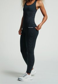 Schwarzes Sport-Top und Leggings mit strukturierten Chevron-Mustern aus elastischem Stoff, kombiniert mit weißen Sportschuhen.