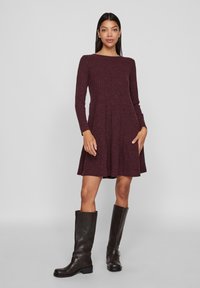Robe longue à manches longues côtelée bordeaux avec une jupe évasée, se positionnant au-dessus du genou. Portez-la avec des bottes en cuir marron jusqu'aux genoux.