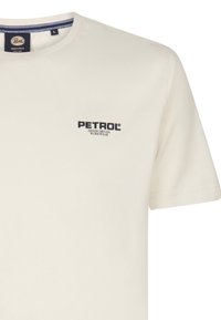 Krémové bavlnené tričko s krátkymi rukávmi a okrúhlym výstrihom. Na ľavej strane hrudi je námornícka modrá značka s nápisom "PETROL" a "DENIM DRIVEN WORKWEAR."