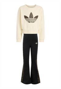 Felpa color crema con design corto e un logo mimetico marrone, abbinata a pantaloni neri a zampa con strisce laterali marroni a motivo animale.