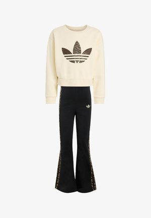 Sudadera color crema con diseño crop y logo de camuflaje marrón, combinada con pantalones negros acampanados con franjas laterales de estampado animal marrón.