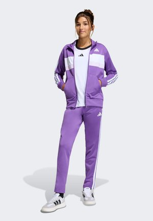 Purple tracksuit featuring a zip-up jacket with white stripes and a matching pant. Includes black and white athletic shoes with accents.