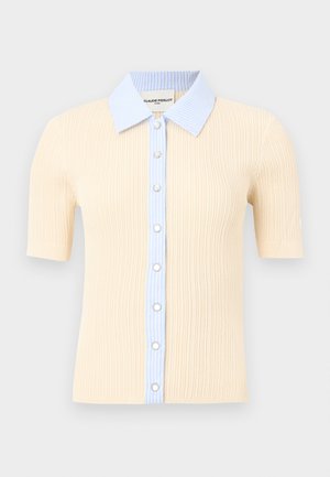 Bež bež majica s kratkimi rokavi in rebrastim pletenim vzorcem, s svetlo modrim ovratnikom s črtami in sprednjo preklopno zadrgo, okrašena z gumbi, ki spominjajo na perle.