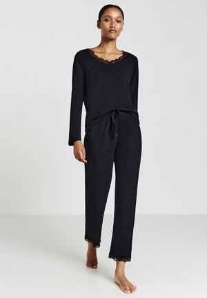 L'ensemble de loungewear noir comprend un haut à manches longues avec un col bordé de dentelle et un pantalon à cordon avec des accents en dentelle à l'ourlet.