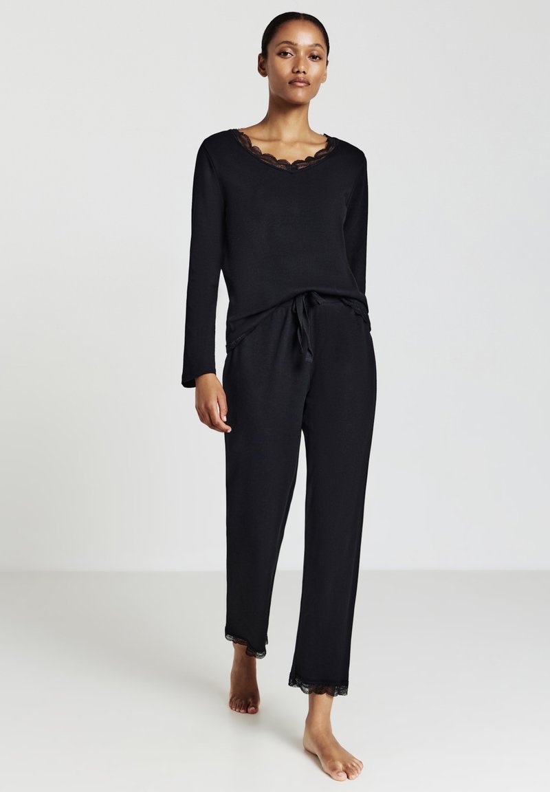 L'ensemble de loungewear noir comprend un haut à manches longues avec un col bordé de dentelle et un pantalon à cordon avec des accents en dentelle à l'ourlet.