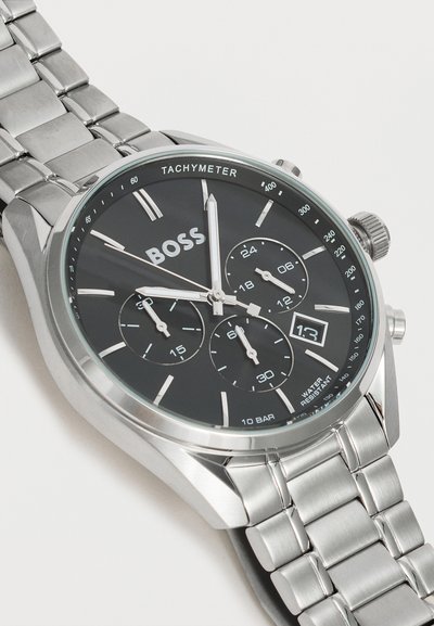 Montre-bracelet en métal argenté avec cadran noir, trois sous-cadrans, échelle tachymétrique, fenêtre date et index ainsi que aiguilles argentés.
