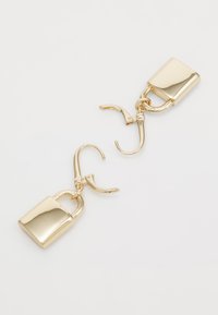 Boucles d'oreilles en métal doré affichant un design de cadenas, avec une surface lisse et polie, suspendues à un fermoir à ressort.