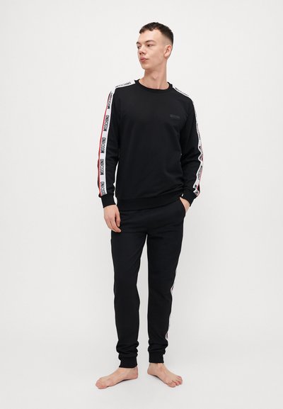 Ensemble sweat-shirt et pantalon noir en coton, featuring des bandes latérales blanches et rouges avec le texte 'MOSCHINO', des poignets côtelés et un col rond.