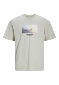 Camiseta beige clara de algodón con un gráfico rectangular que presenta un paisaje urbano y el texto "Originals Studio" en negro.