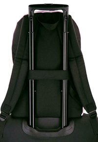 Mochila negra asegurada en el mango telescópico extendido de una maleta con ruedas, mostrando las correas acolchadas y la banda de soporte.