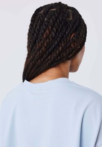 Lichtblauw sweater met een subtiele textuur, zichtbaar van achteren, gecombineerd met lange, stevig gevlochte donkere vlechten.