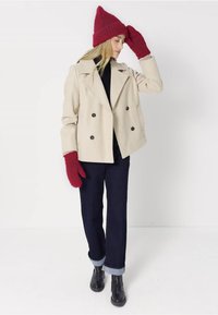 Beige dubbelzijdig jasje, zwarte coltrui, donkerblauwe jeans met opgerolde manchetten, rode gebreide beanie en bijpassende wanten. Zwarte enkellaarsjes.