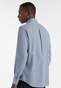 Uomo che indossa una camicia a maniche lunghe a quadretti blu e bianchi, visto di spalle e leggermente girato di lato.