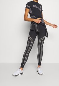 Svart träningsoutfit bestående av en figursydd kortärmad topp och högmidjade leggings med reflekterande detaljer och ett meshnätmönster. Vita sneakers.
