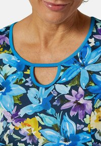 Blumen Kurzarm-Oberteil mit leuchtend blauen, lila und gelben Blumen auf dunklem Hintergrund. Schlüssel-ausschnitt mit türkisfarbener Naht.
