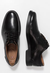 Chaussures en cuir noir avec un bout arrondi, un laçage, une texture lisse et une semelle intérieure contrastante de couleur marron clair. Semelle en caoutchouc noir robuste.