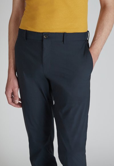 Granatowe spodnie o gładkiej fakturze, z zapięciem na guzik i kieszeniami po bokach. Połączone z dopasowanym żółtym topem.