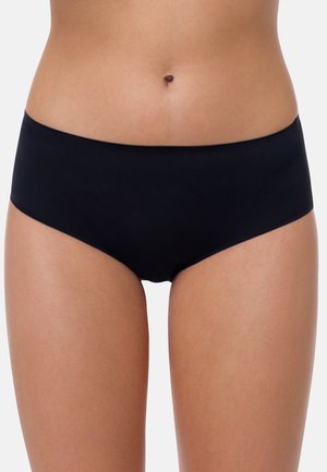 Woman wearing plain black hipster-style underwear, shown from waist to upper thighs against a light gray background.