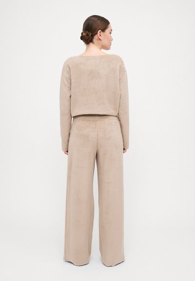 Beige, soft fabric lounge set with a cropped top and wide-leg pants. The top features a rounded back neckline and relaxed fit.