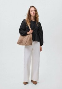 Crna bluzica s napuhanim rukavima od teksturiranog materijala, bijele široke hlače s bočnim gumbima i smeđa meka torba. Smeđa obuća upotpunjuje izgled.