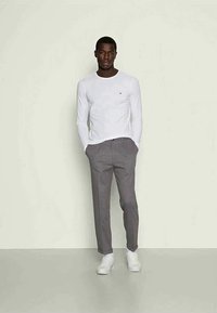 Biela košeľa s dlhým rukávom a okrúhlym výstrihom, doplnená o šedé nohavice na mieru a biele tenisky, s jednoduchým, klasickým dizajnom.