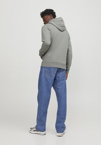 Gray hooded sweatshirt with a kangaroo pocket, paired with loose blue denim jeans. The fabric appears soft with a smooth texture.